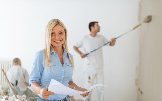 Smiling woman overseeing a home renovation project with workers painting the walls, highlighting property renovations in Phuket to increase rental appeal.